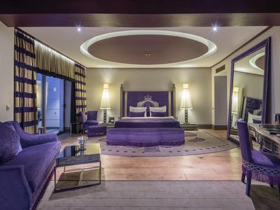 Habitación de hotel elegante con esquema de color violeta, cama grande, sofá, escritorio y televisor de pantalla plana.