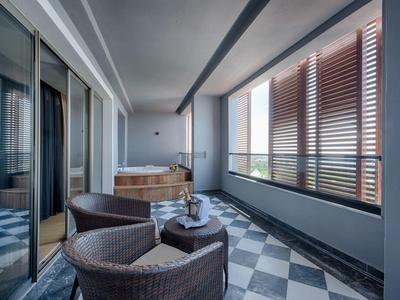 Balcón moderno con sillas cómodas y pantalla de madera, jacuzzi visible en el interior.