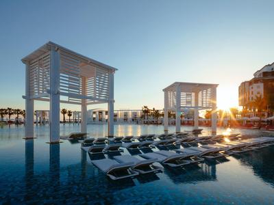 Moderna piscina exterior con tumbonas, pabellones y puesta de sol en el hotel.