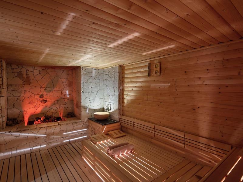 Sauna acogedora con revestimiento de madera, horno de piedra calefaccionado y toallas relajantes.
