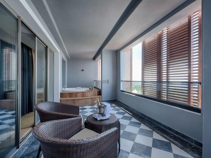 Balcón moderno con sillas cómodas y pantalla de madera, jacuzzi visible en el interior.