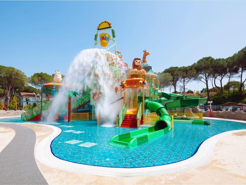 Parque acuático con toboganes y piscina bajo un cielo azul claro, rodeado de árboles.