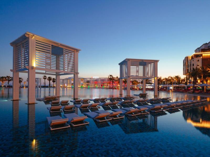 Piscina de lujo con tumbonas y pabellones al atardecer en un resort hotelero.