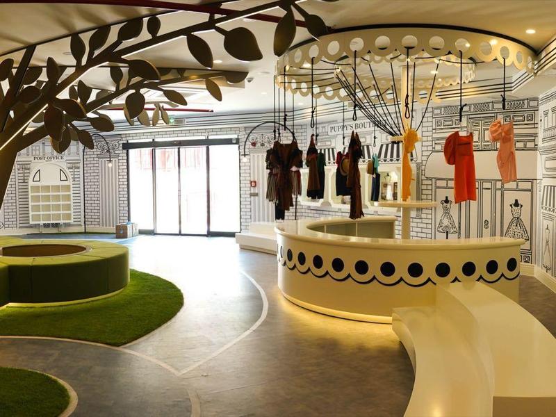 Área moderna del vestíbulo del hotel con asientos redondos, gran araña y murales estilizados.