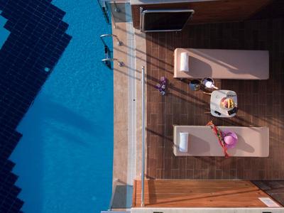 Letecký pohled na bazén a dřevěnou terasu se dvěma lehátky a stolkem.