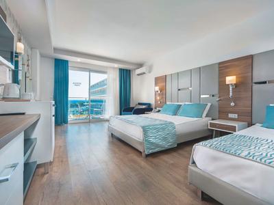 Modernes Hotelzimmer mit zwei Betten, Holzboden, Flachbildschirm und Balkon mit Meersicht.