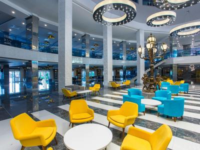 Velká moderní hotelová hala se žlutými a modrými křesly, kulatými stoly a kruhovými lustry.