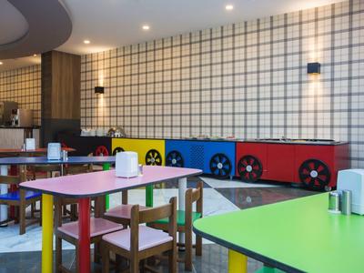 Barevná herna se zelenými, červenými a fialovými stoly a dřevěnými židlemi.