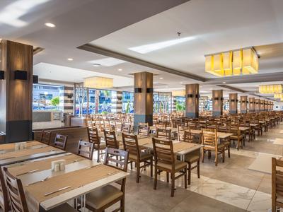 Velká hotelová jídelna s dřevěnými stoly a židlemi uspořádanými v řadách.