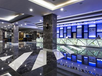 Moderní hotelová hala s lesklou podlahou a modře osvětlenou recepcí.