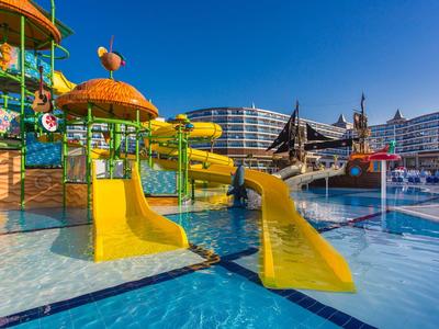 Žluté vodní skluzavky v hotelovém bazénu pod jasně modrou oblohou.