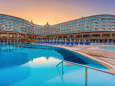 Moderní hotel s velkým bazénem při západu slunce a lehátky podél okraje.