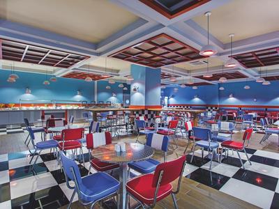 Barevná jídelna s červenými a modrými židlemi a černo-bílou šachovnicovou podlahou.