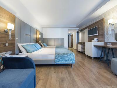 Moderní hotelový pokoj s manželskou postelí, modrým gaučem a světlou dřevěnou podlahou.