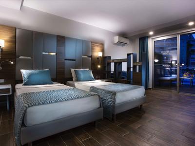 Moderní hotelový pokoj se dvěma jednolůžky a výhledem na město přes velké okno.