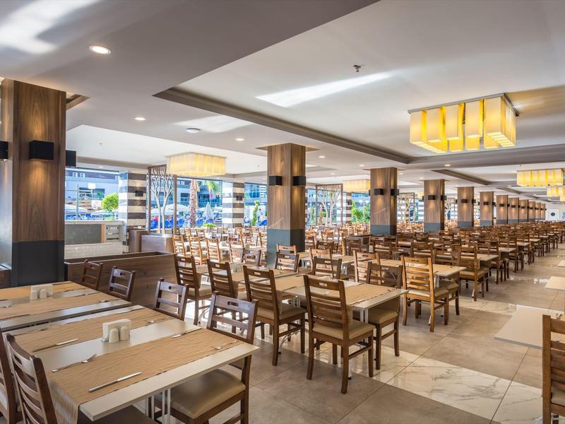 Velká hotelová jídelna s dřevěnými stoly a židlemi uspořádanými v řadách.