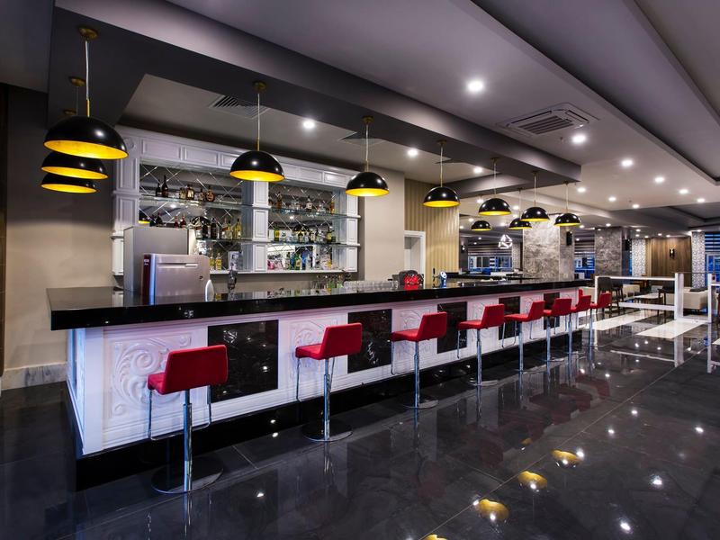 Moderní bar s červenými stoličkami a žluto-černými závěsnými světly.