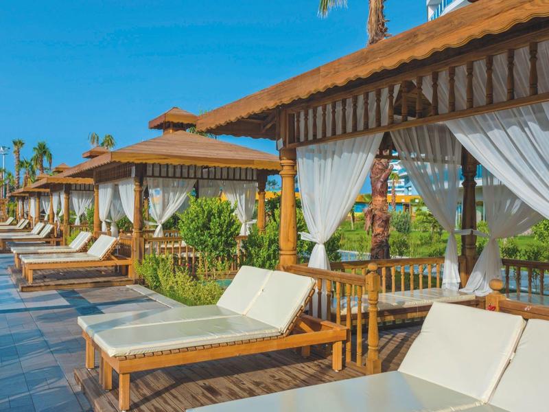 Venkovní relaxační zóny s lehátky a dřevěnými altány pod modrou oblohou.