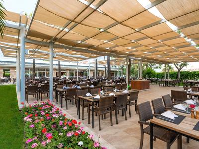 Restauracja na świeżym powietrzu z zadaszonym miejscem do siedzenia i drewnianymi meblami w ogrodzie hotelowym.