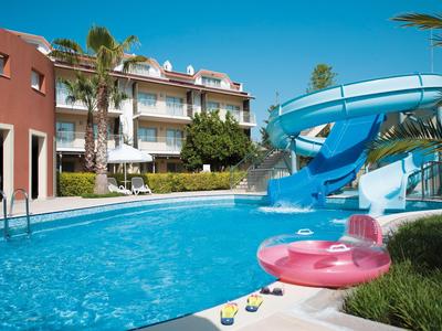 Basen z zjeżdżalnią i dmuchanym kołem przed budynkiem hotelu w słoneczny dzień.