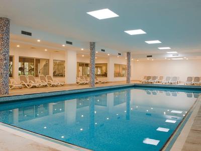 Kryty basen z niebieską wodą, leżakami i kolumnami w strefie spa hotelu.