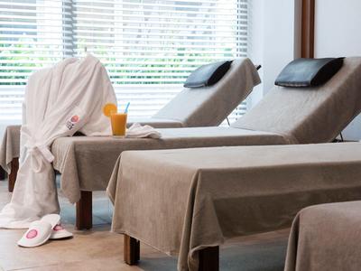 Strefa relaksu z leżankami do masażu, szlafrokiem, kapciami i sokiem przed dużymi oknami z roletami