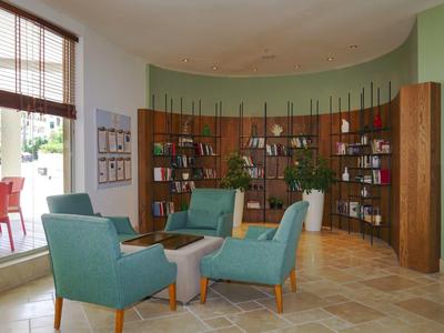 Przytulny hotelowy salon z niebieskimi fotelami i drewnianymi półkami.