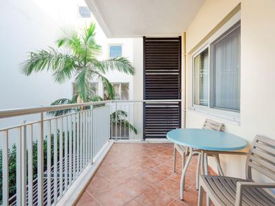 Balkon z stołem i krzesłami obok okna, tropikalna roślina w tle.