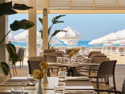 Restauracja z nakrytymi stołami nad brzegiem plaży i białymi parasolami w tle.