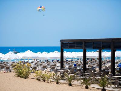 Piaszczysta plaża z leżakami, parasolami i drewnianą pergolą nad morzem.