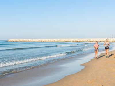 Dwie osoby biegną brzegiem plaży, w tle spokojne morze i czyste niebo.
