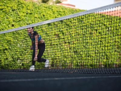 Osoba grająca w tenisa na zewnętrznym korcie z zielonym tłem.