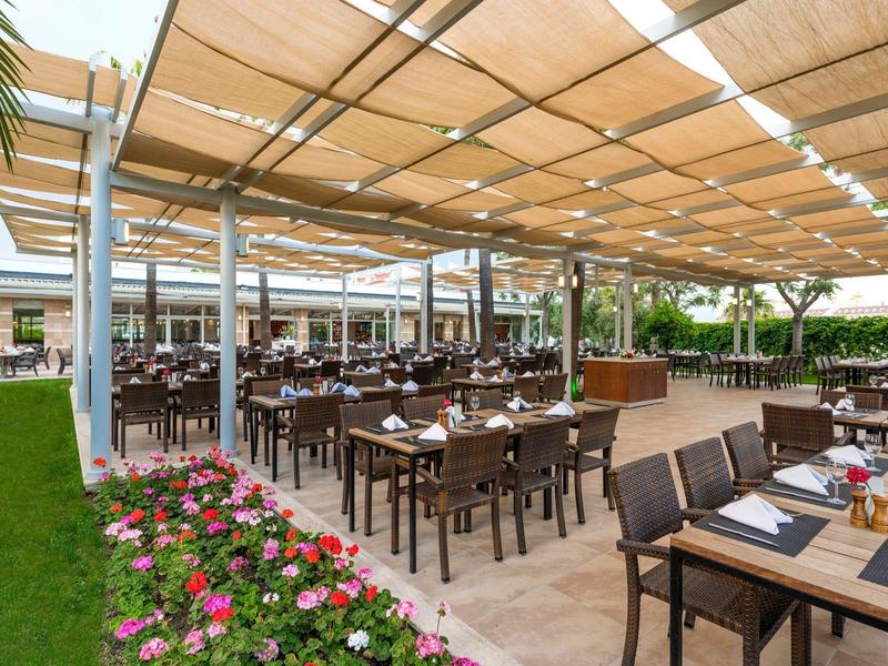 Restauracja na świeżym powietrzu z zadaszonym miejscem do siedzenia i drewnianymi meblami w ogrodzie hotelowym.
