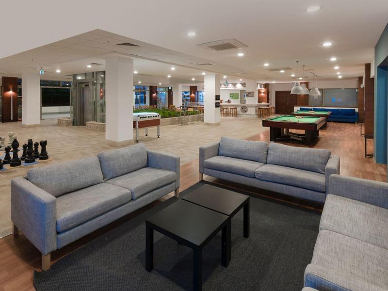 Nowoczesny salon hotelowy z sofami, stołami do bilarda i dużą szachownicą na podłodze.