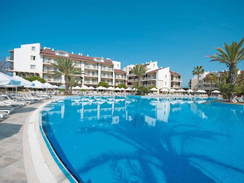 Duży basen na zewnątrz z leżakami przed budynkiem hotelu przy czystym niebie.