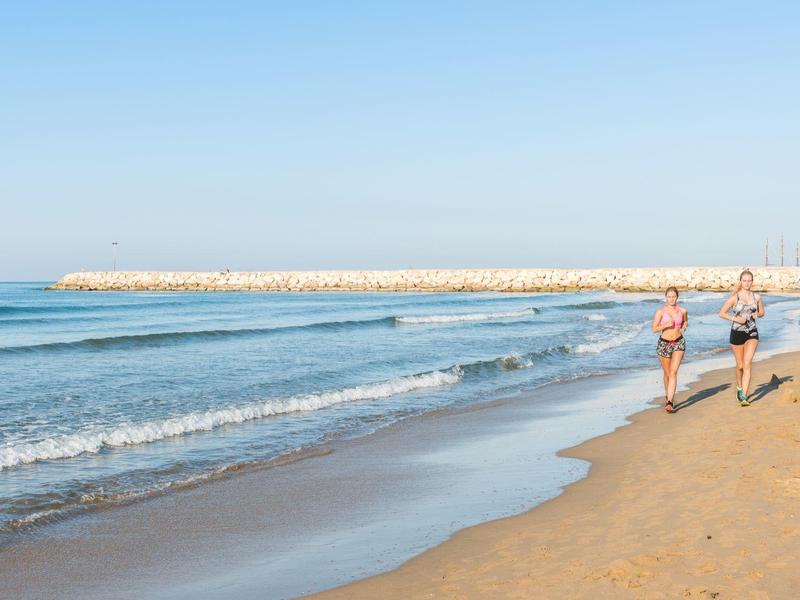 Dwie osoby biegną brzegiem plaży, w tle spokojne morze i czyste niebo.