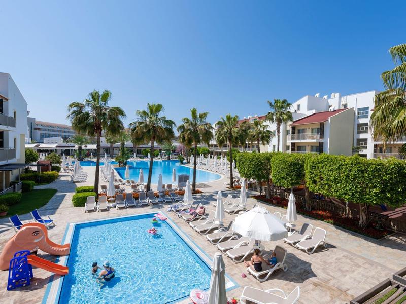 Nowoczesny hotelowy basen z parasolami, leżakami i palmami pod bezchmurnym, niebieskim niebem.