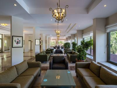 Bright hotel lobby with sofas, plants, and chandeliers next to large windows.