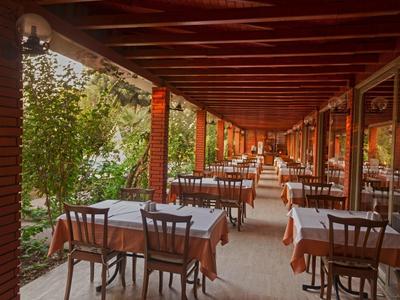 Covered outdoor terrace with tables and chairs, surrounded by green plants.