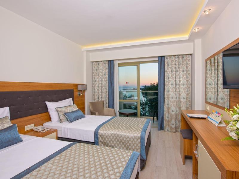 Modern hotel room with two single beds, balcony view, and wall-mounted TV.