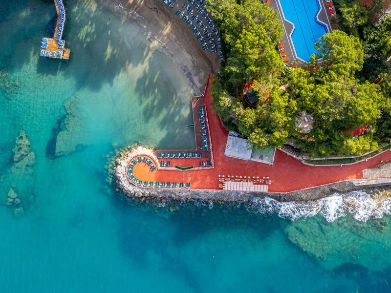 Aerial view of a hotel with pool, terrace, and clear blue sea water