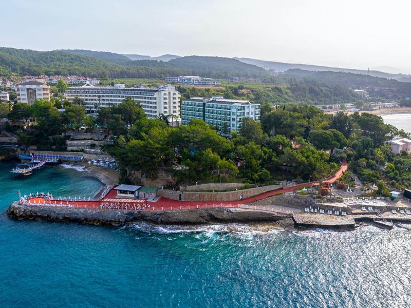 Aerial view of a coastal resort with green trees, buildings, and a pier in the blue sea.