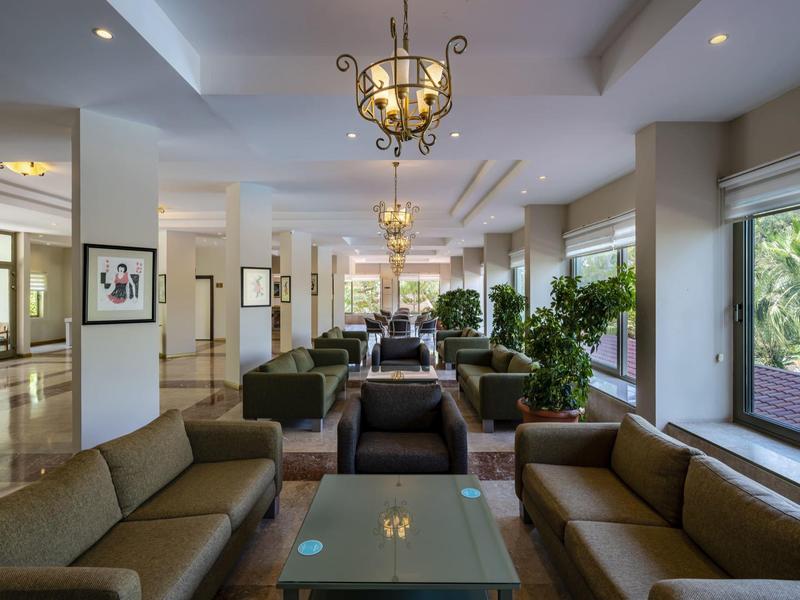 Bright hotel lobby with sofas, plants, and chandeliers next to large windows.