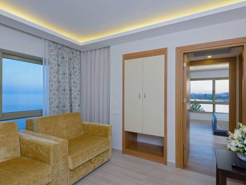 Hotel room with two yellow armchairs, sea view, and adjacent balcony.