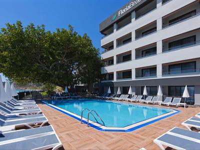 Moderner Poolbereich mit Liegestühlen und einem Baum neben einem mehrstöckigen Hotel.