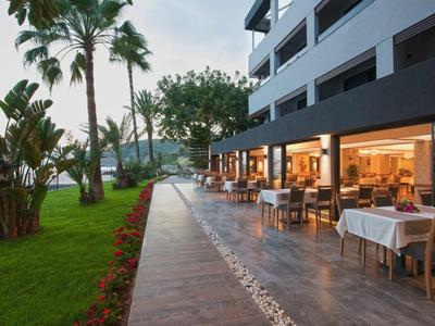 Außenbereich eines Restaurants mit Tischen und Stühlen neben einem Hotel und Blick auf Palmen.