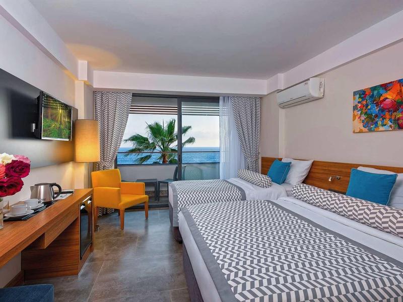 Modernes Hotelzimmer mit zwei Betten, buntem Wandbild, Fernseher und Balkon mit Meerblick.