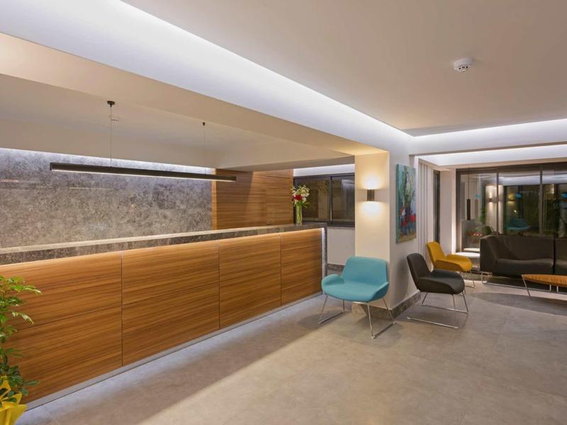 Moderner Empfangsbereich mit Holztheke, LED-Beleuchtung, Pflanzen und bequemen Sesseln.