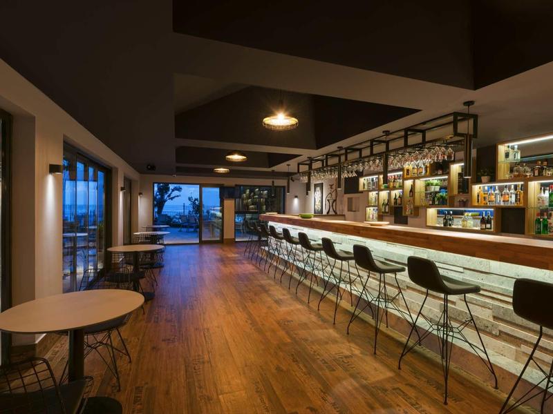 Moderner, langer Barraum mit Holzboden, vielen Barhockern und warmen Beleuchtungselementen.