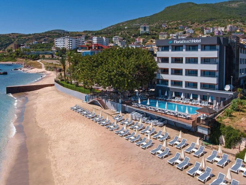 Strand mit Liegestühlen, blauer Meerblick und angrenzendem mehrstöckigem Hotelgebäude im Hintergrund.